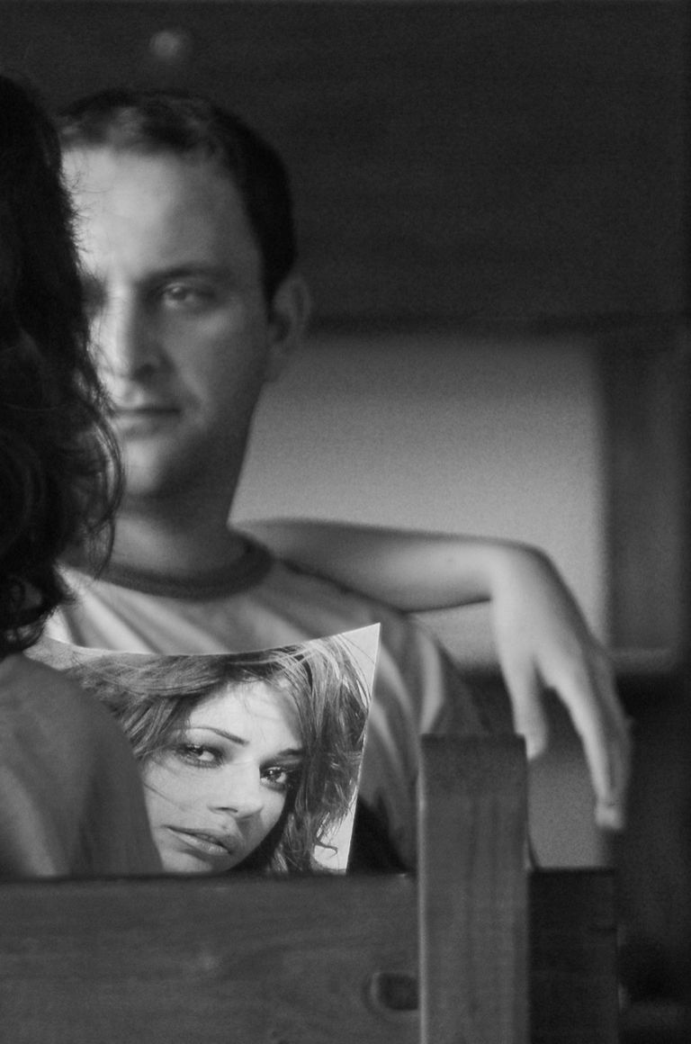 Black & white image of girl looking at a magazine with a man sat in the background. Zakynthos